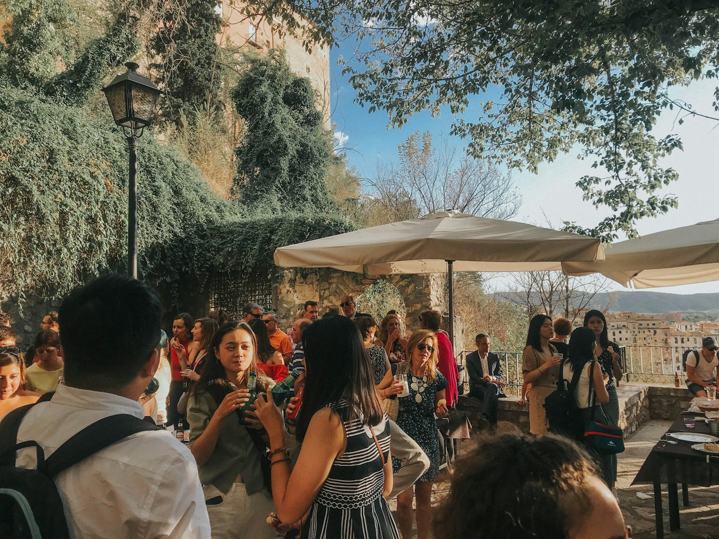 People socializing outdoors on a sunny terrace with ivy walls.