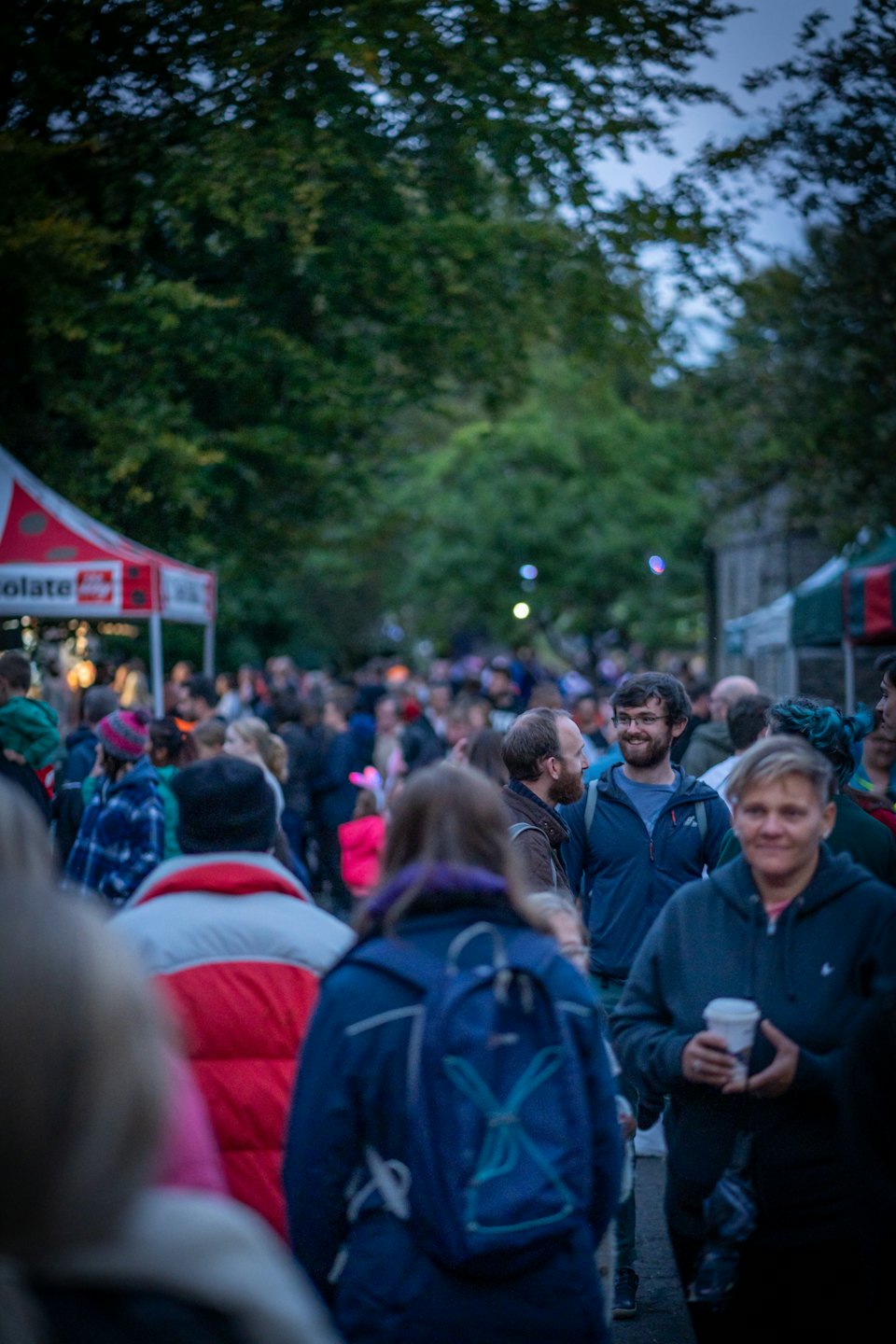 People socialize at a busy outdoor market with vendor tents.