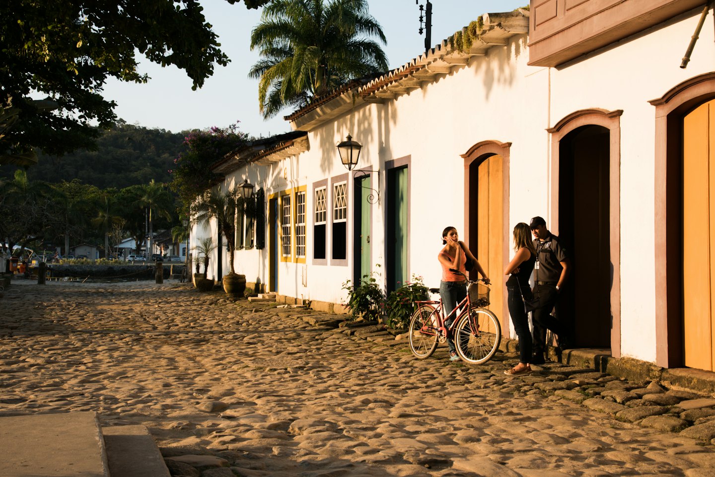 Three friends conversing on a cobblestone street near colonial buildings.