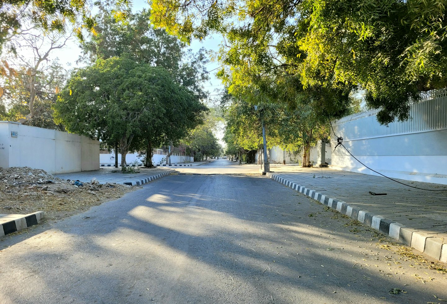 Empty residential street lined with trees and white walls.