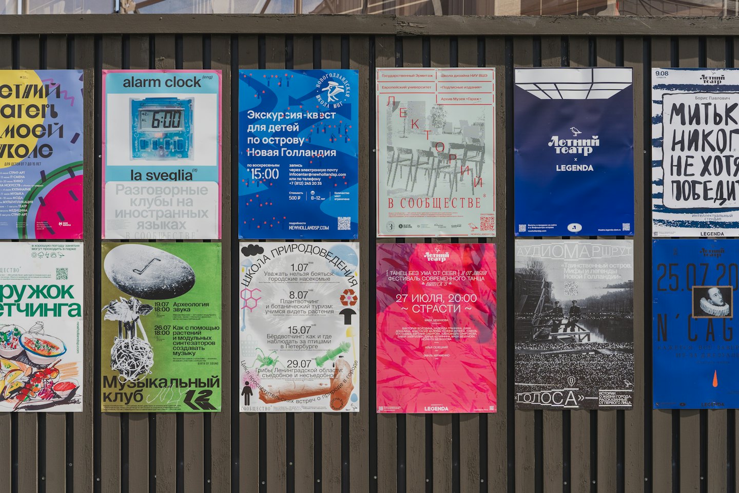 Public bulletin board covered in various event posters on a fence.